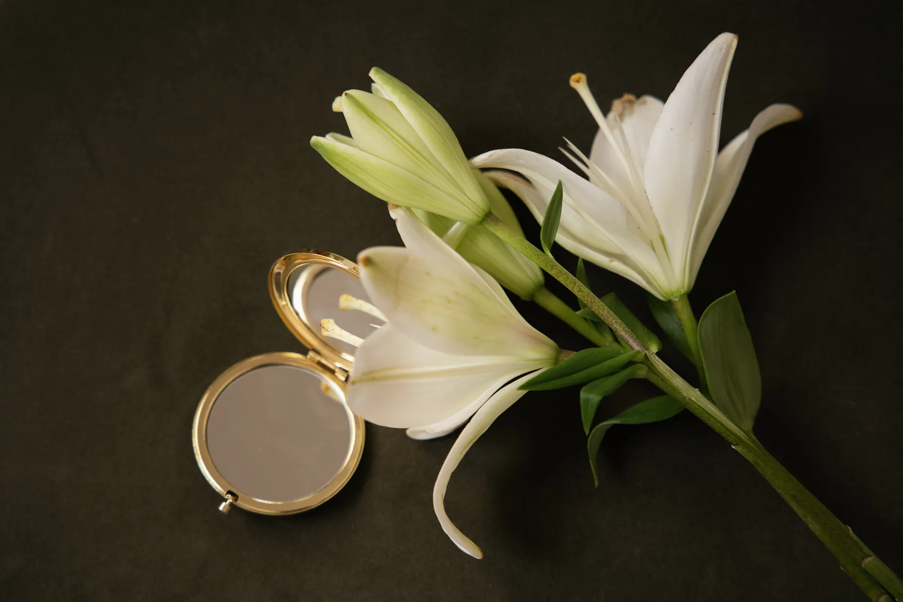 White lilies beside an open gold compact mirror